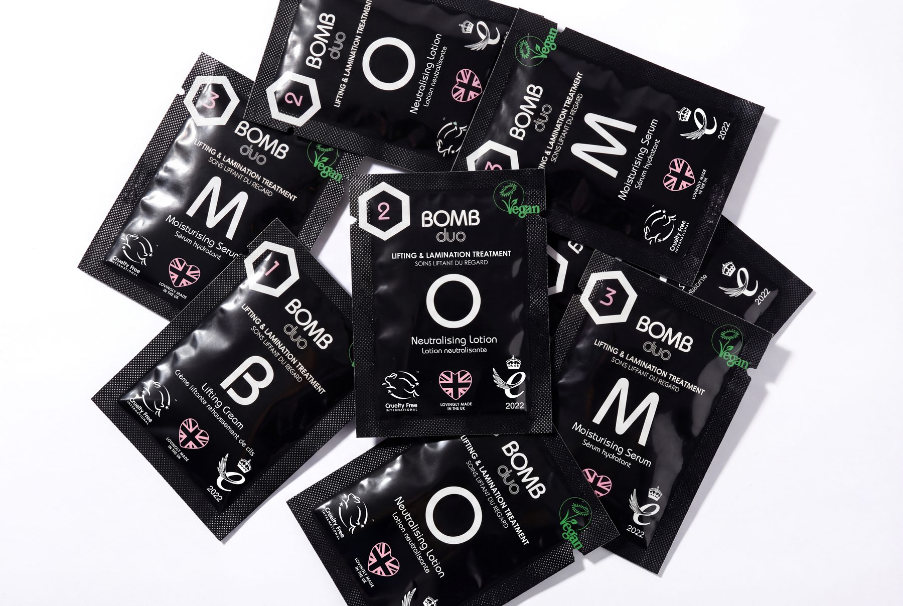 BOMB Duo single-use treatment sachets scattered on a white surface