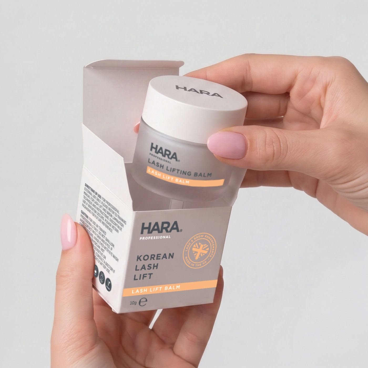 Hands opening a HARA Professional Korean Lash Lift balm box to reveal the frosted jar